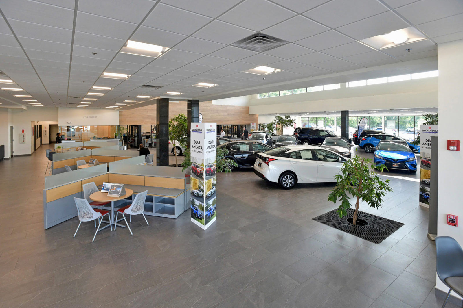 Car showroom showing a line of Herman Miller Canvas workstations and seating on the left side. Showroom cars are along right side of picture.