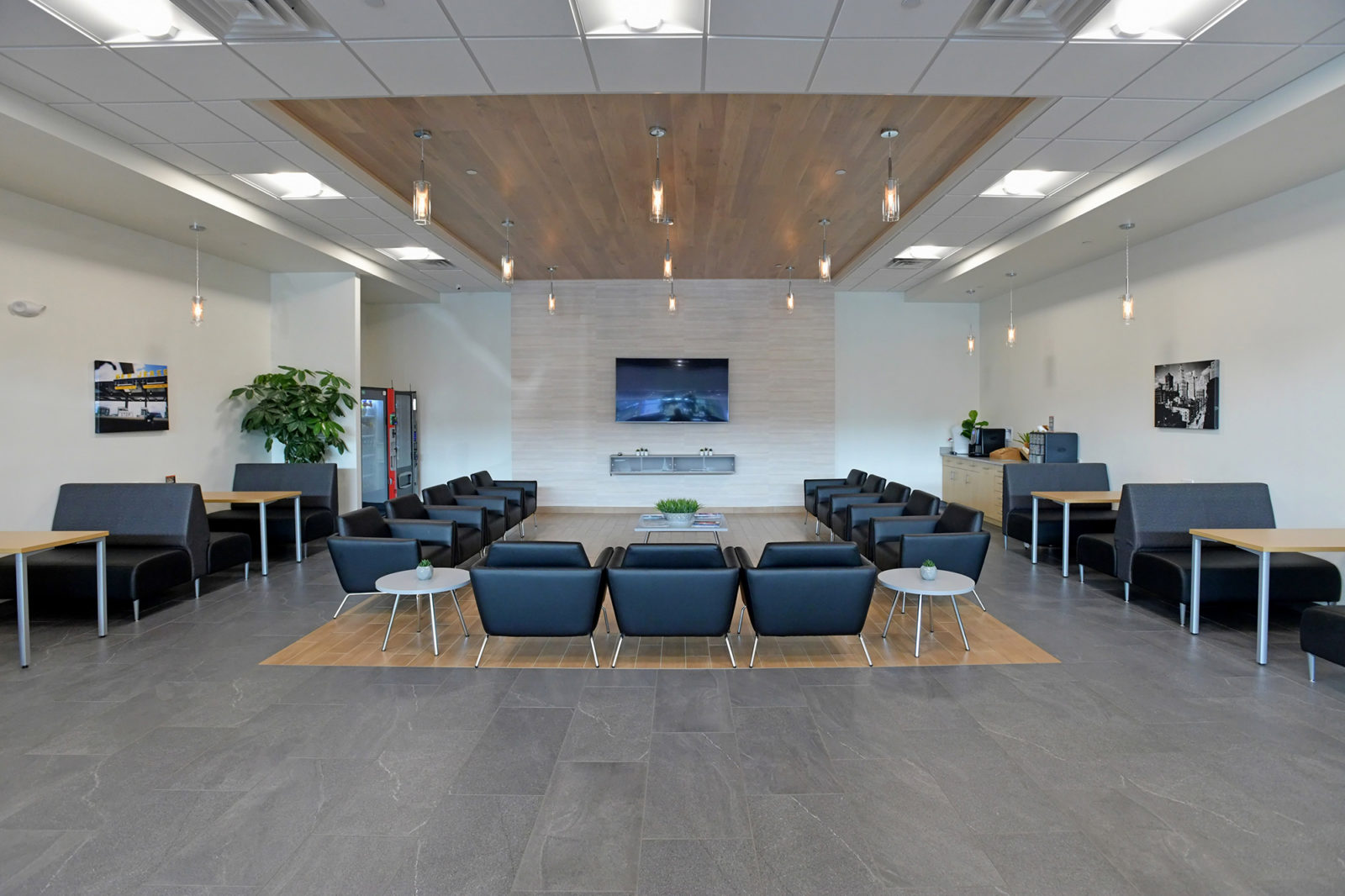 Waiting area of car dealership. Booths and tables line the outer walls and single black leather club chairs form a U-shape area in the center of the room.