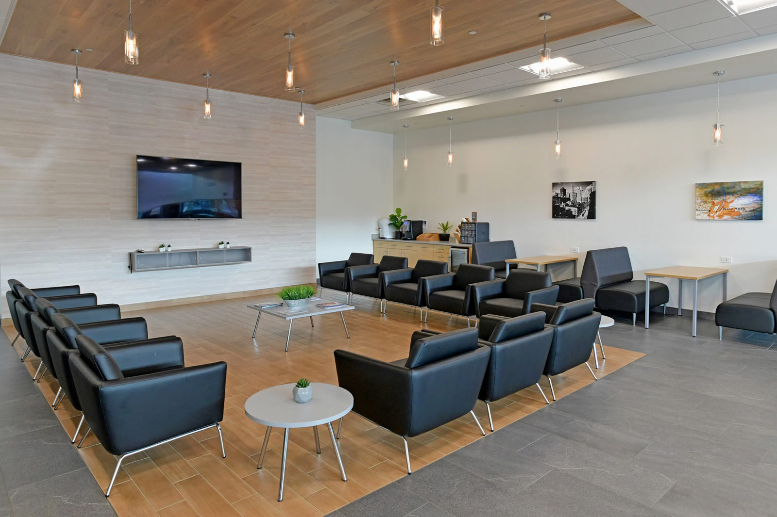 Waiting area at car dealership. Black club chairs lined up in a U-shape gathered around a coffee table. There are booths along the back wall.