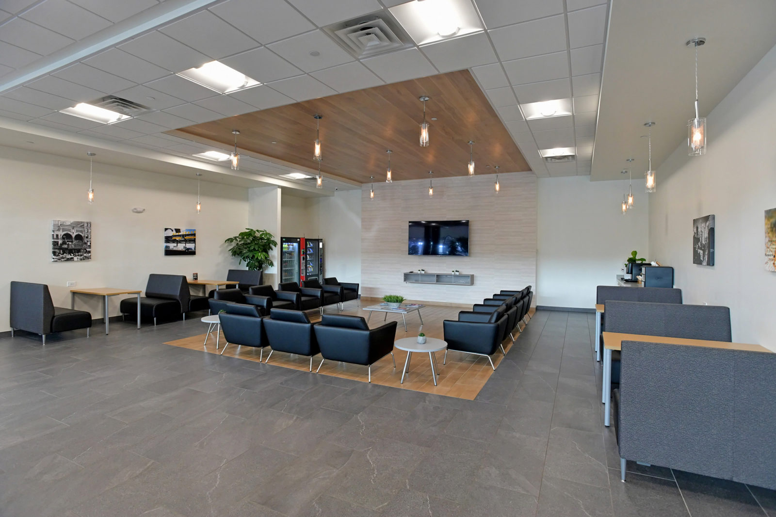 Waiting area of car dealership with booths along the walls and a cluster of black leather club chairs in the center of the room.