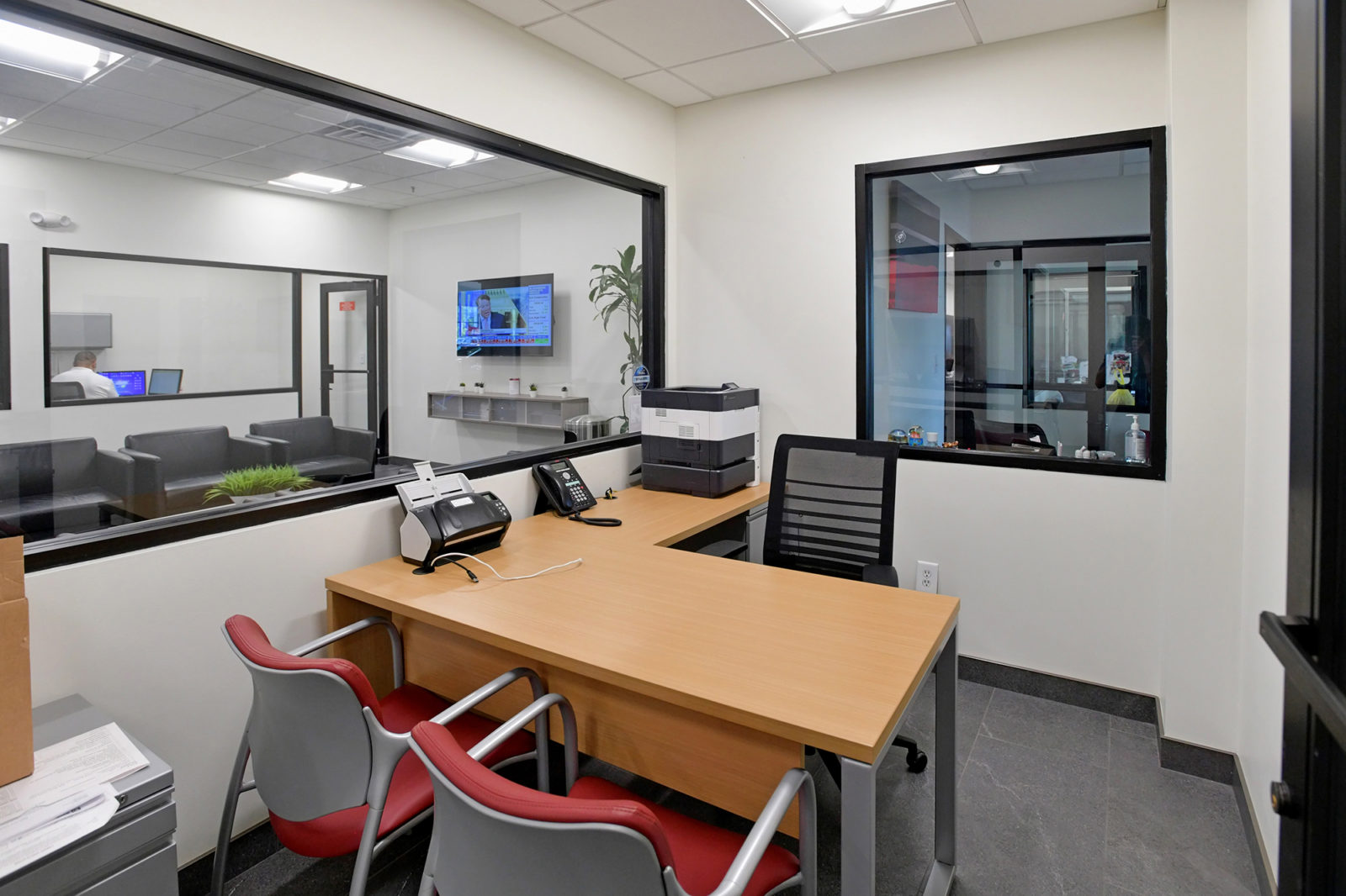 Private office with L-shape wood-grain desk, 2 red guest chairs and black task chair. There are 2 large windows in the office.