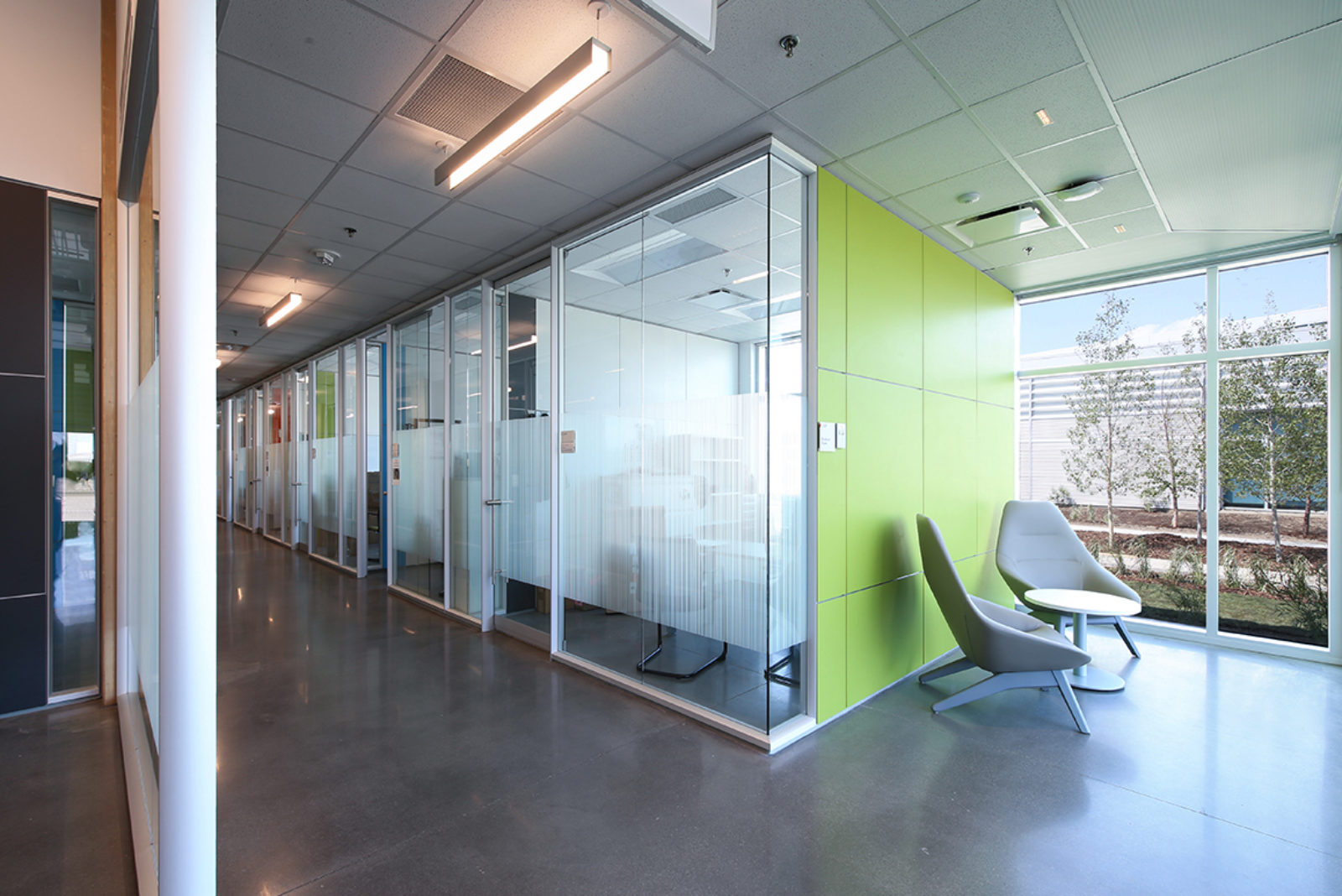 Modular construction solution - view of exterior corner. Bright green panels on one side, glass sliding doors along hallway.