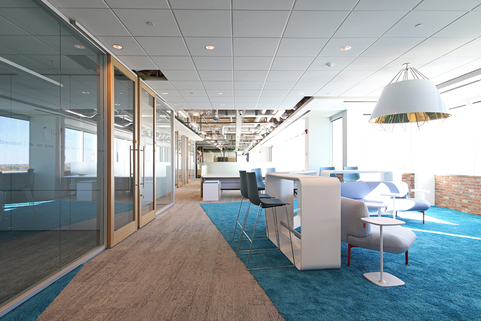 Bright space with DIRTT walls and doors along left side; a collection of lounge and collaborative furniture on right side of room, with a bright blue rug