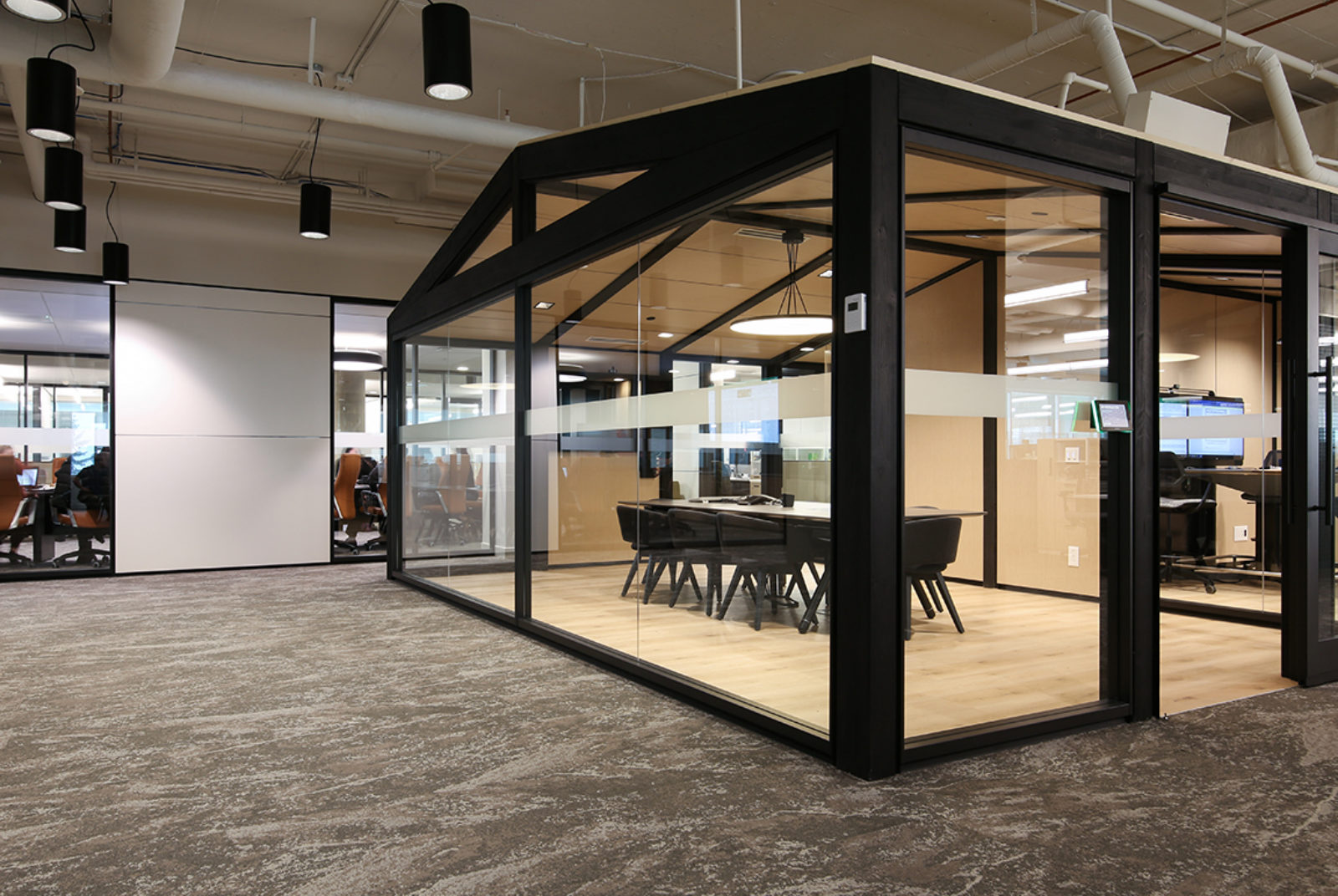Room with exposed ceilings, carpet and freestanding DIRTT solution.  Conference area has glass walls, thick black beams, light wood interior
