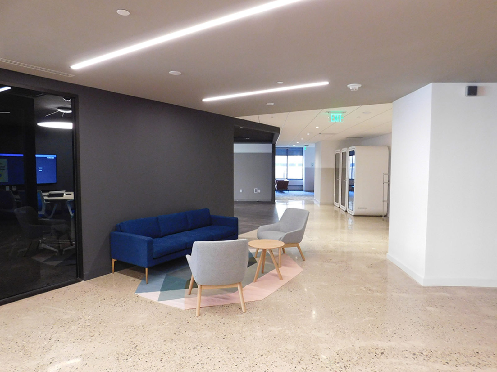 Lobby area with blue fabric sofa, light grey lounge chairs with small wooden tables in middle