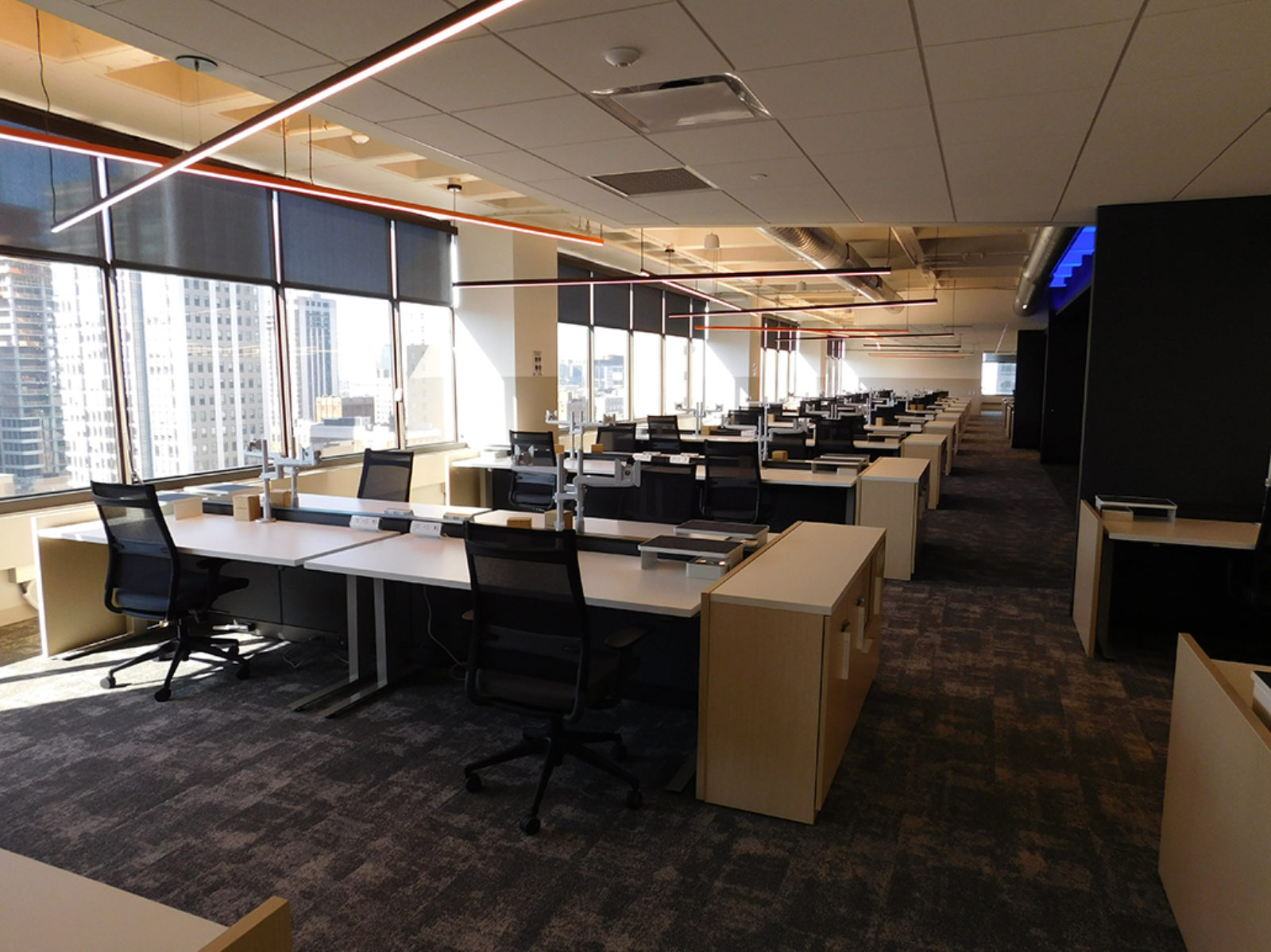 Height-adjustable benching workstations with black task chairs and recycling units at end of stations