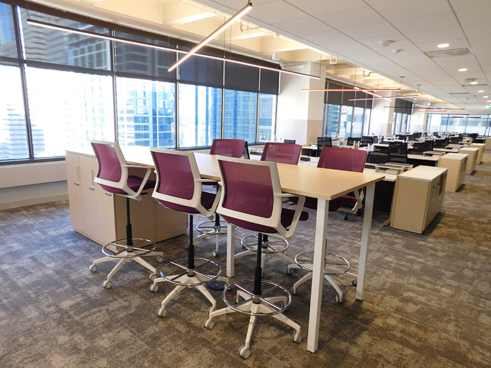 Collaborative table with burgundy mesh stools, clusters of workstations in background
