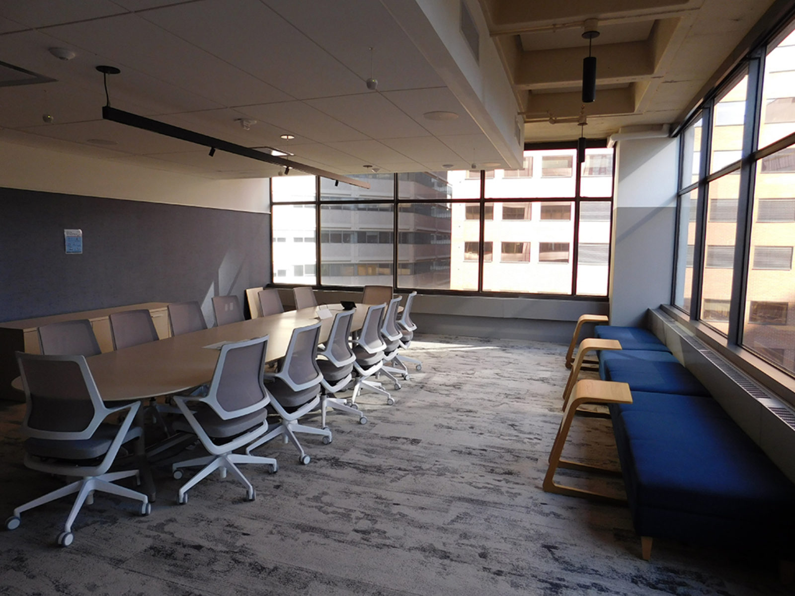 Large conference room with blue fabric benches under windows, large wooden table with grey mesh chairs