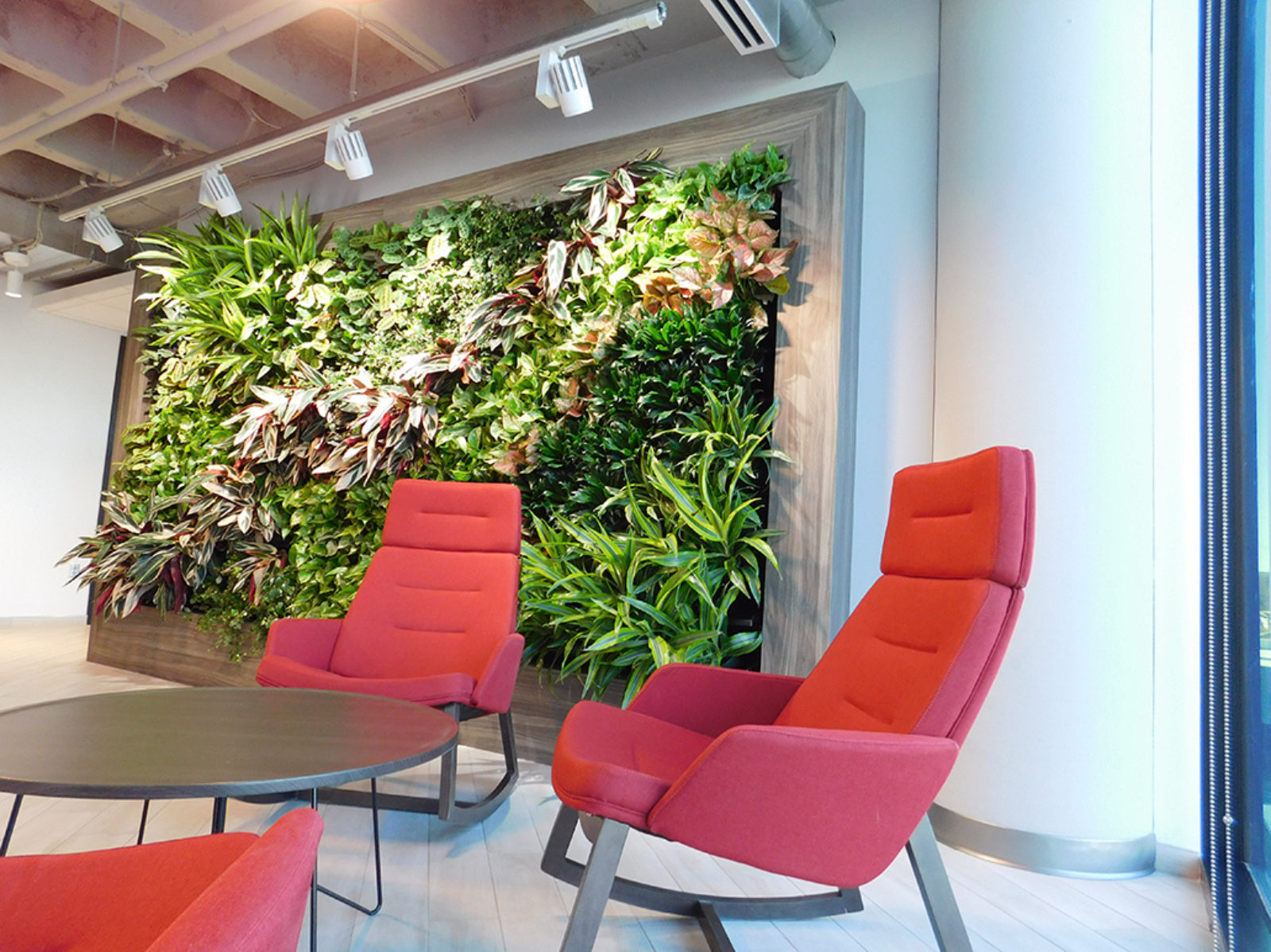 Living wall with red, upholstered, high back lounge chairs and wooden round table.