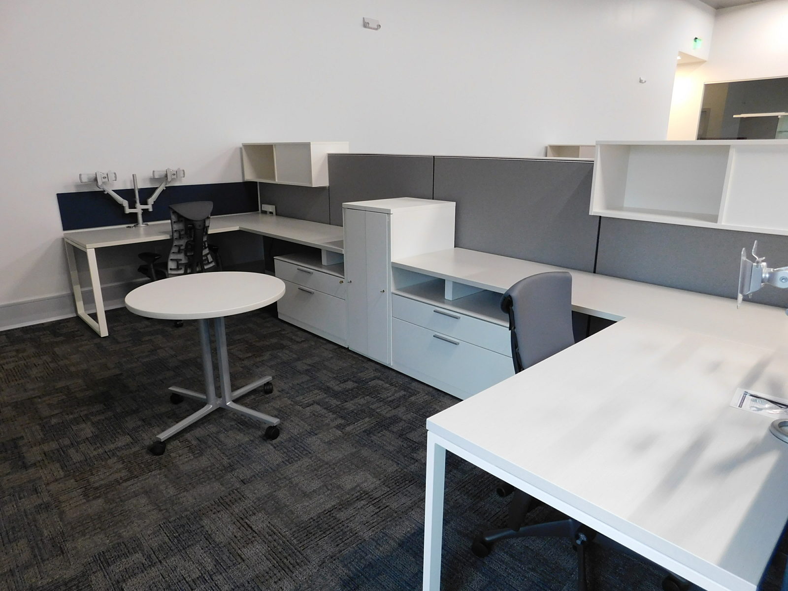 Herman Miller workstations with white surfaces and storage, grey fabric panels, small round table in between