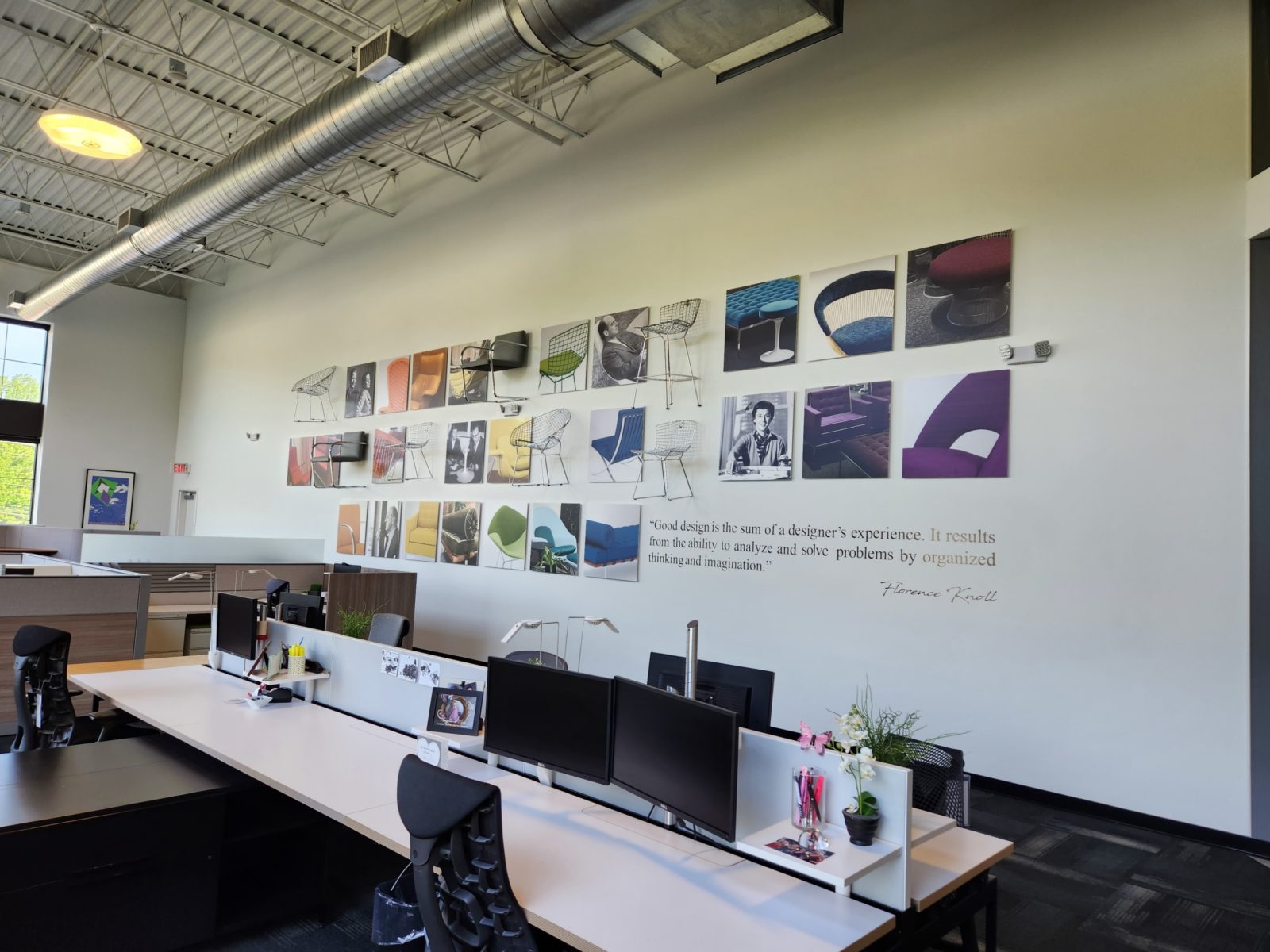 An office with a lot of pictures on the wall.  Pictures are of furniture pieces and designers creating a gradient of colors from red to purple.