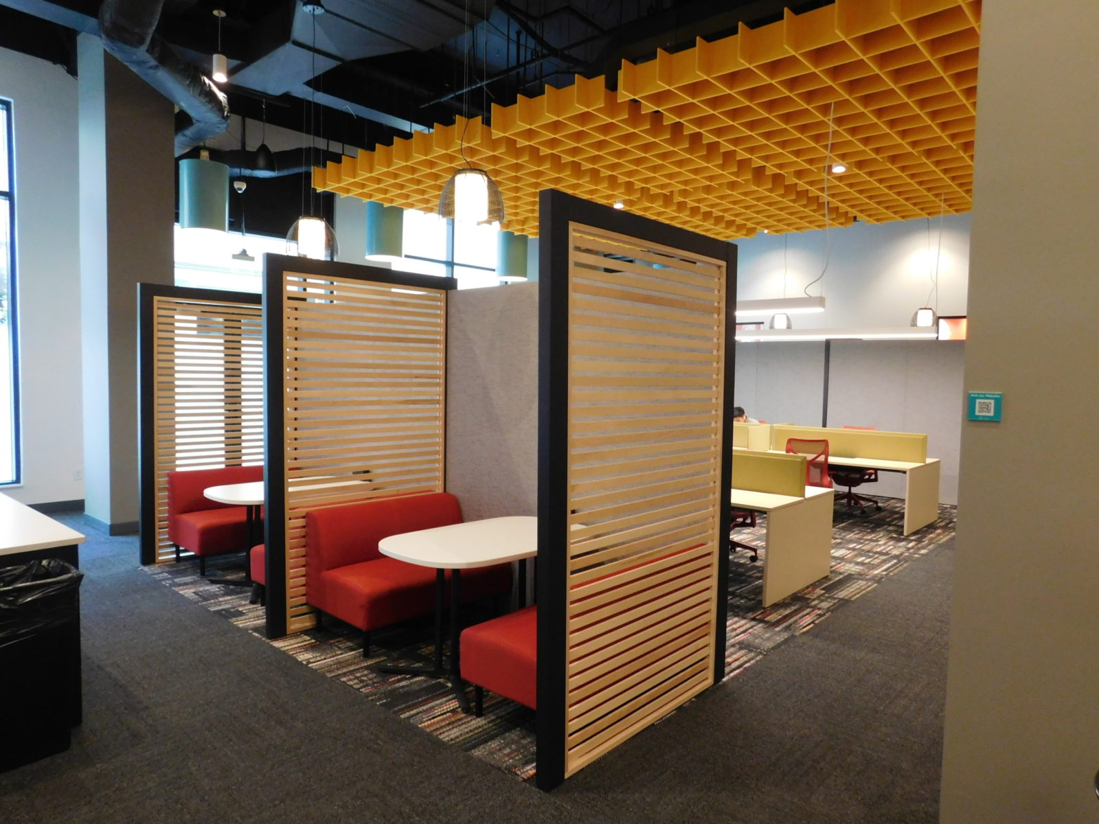 Co-working space showing 2 Herman Miller Overlay rooms with wood slat walls on the side and red booths with tables inside. Workstations in the background.