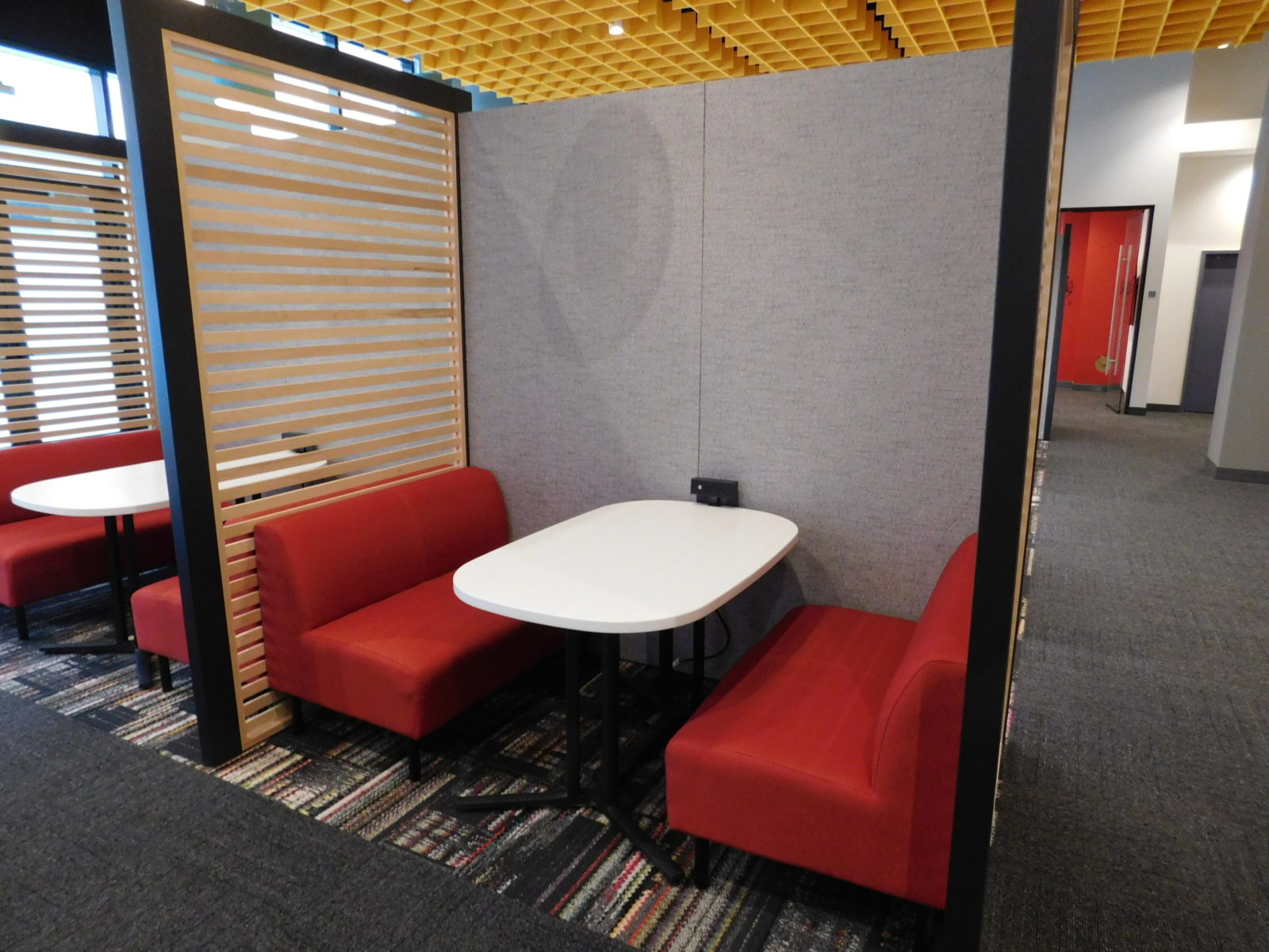 Interior of a Herman Miller Overlay unit. Two identical units side-by-side, with red fabric 2-seater booths on either side of a white table.