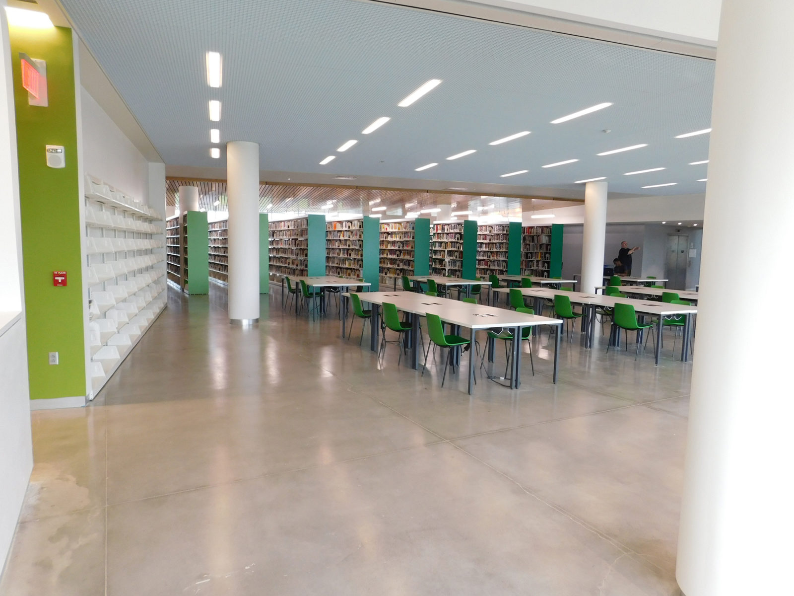 View of the Temple library bookshelves and some collaborative tables and chairs. Bookshelf ends are painted in different shades of green.