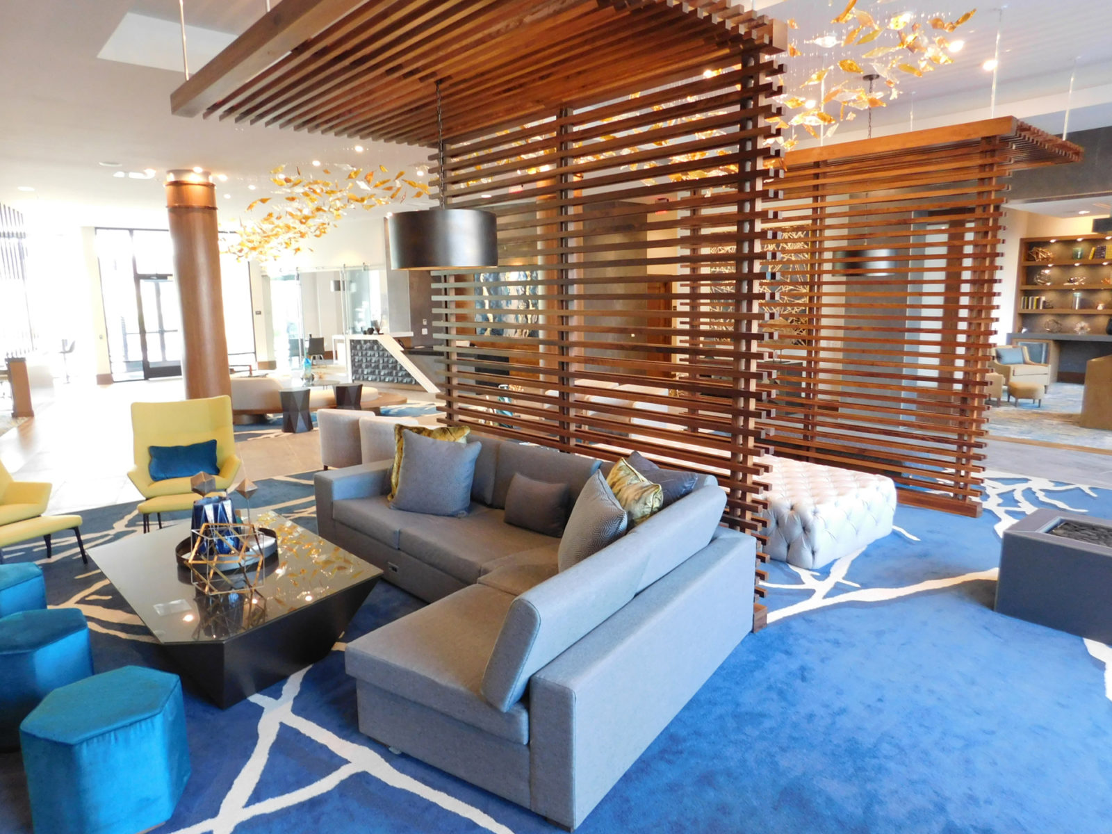 Common lobby space in building with a variety of lounge furniture throughout. Wooden slat wall and trellis are featured