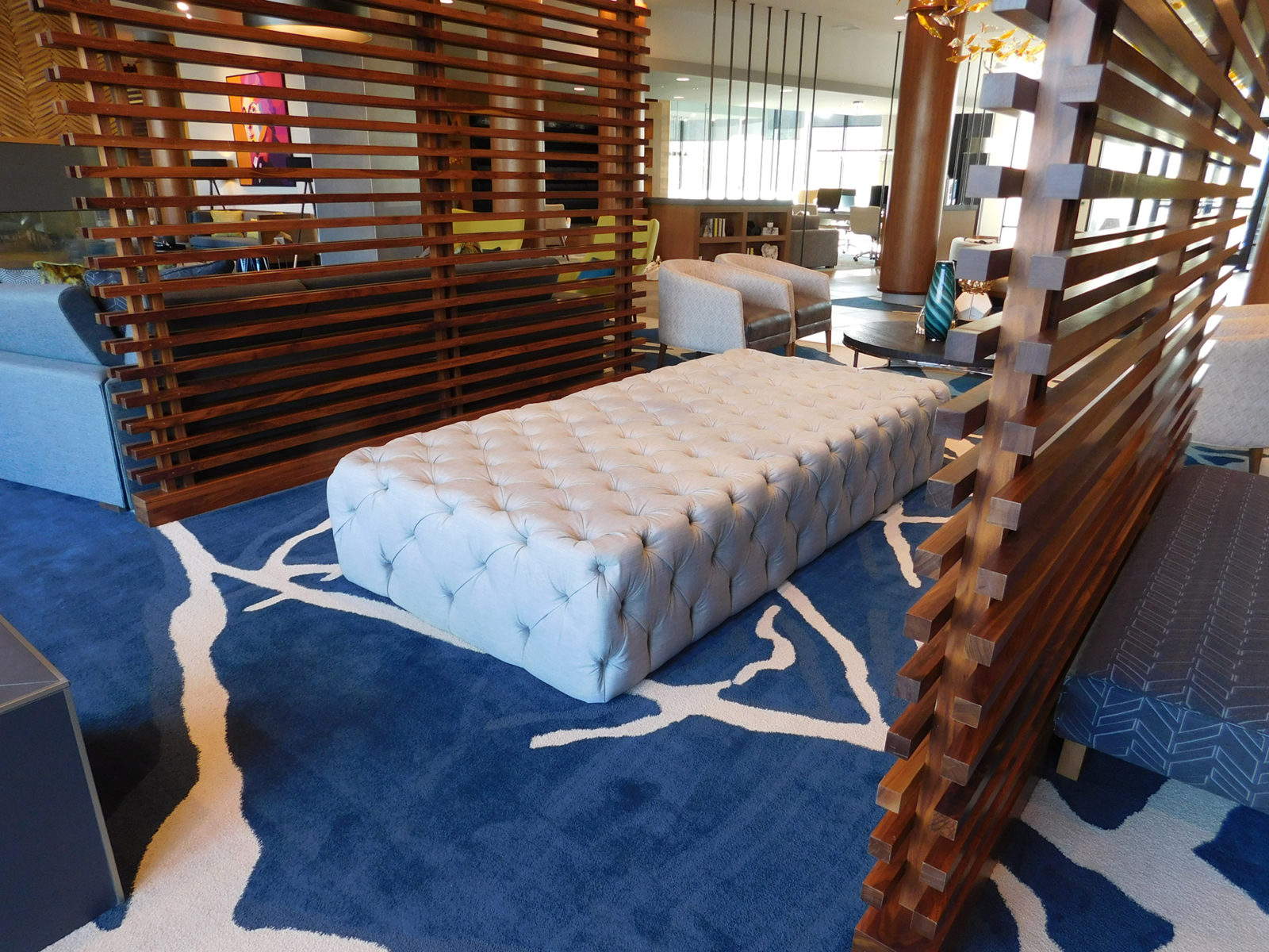 Image of a light color upholstered bench in the center of the lobby. The bench is tufted all over to create depth and dimension to the fabric