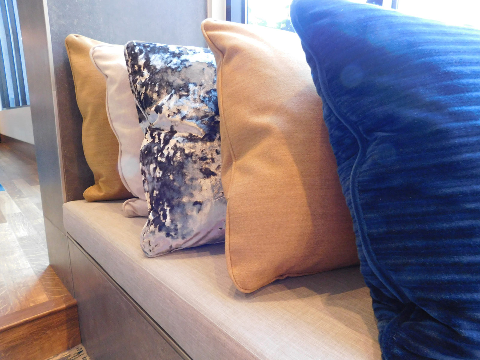 Detail image of a row of pillows lined up on a bench. The pillows are a combination of blue, white and tan colors.