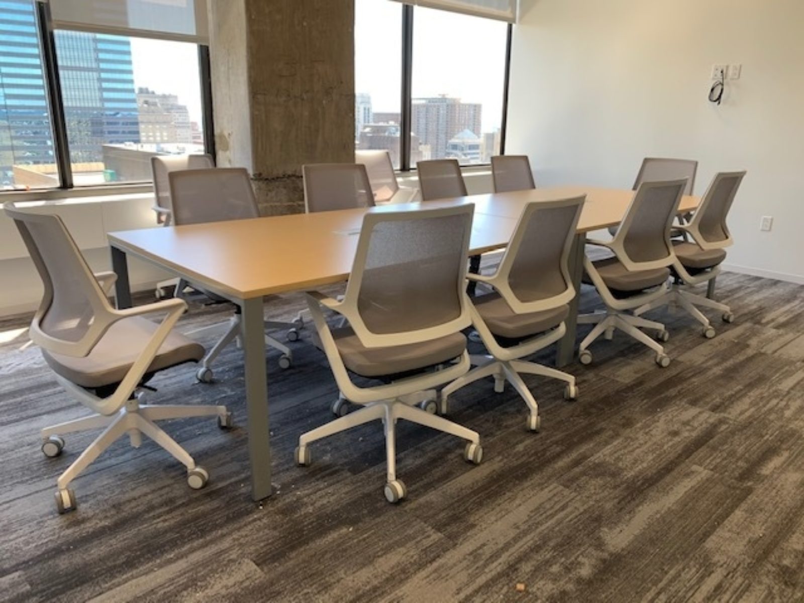 Conference room with woodgrain table top and silver legs. Conference chairs have grey mesh backs and grey seats with white frames.