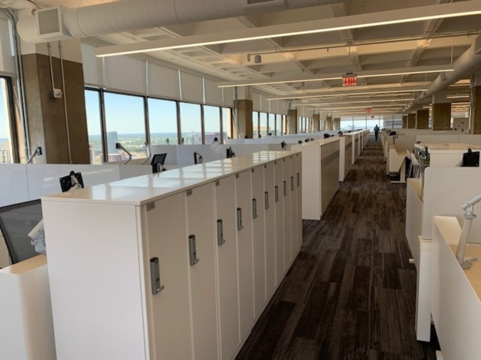Open area with rows of lockers on the ends of workstation clusters. Neutral and clean color palette throughout the space.