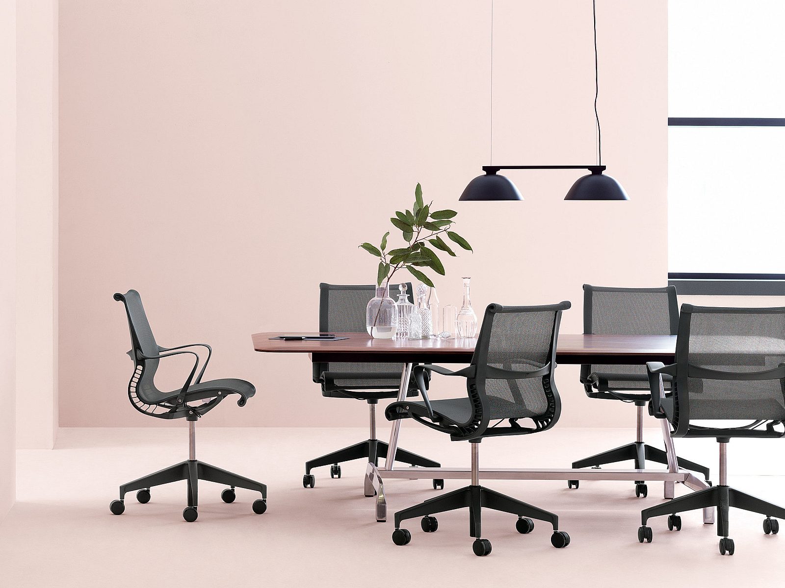 Light pink room (walls and floor) with dark Herman Miller Setu chairs around a Herman Miller conference table.
