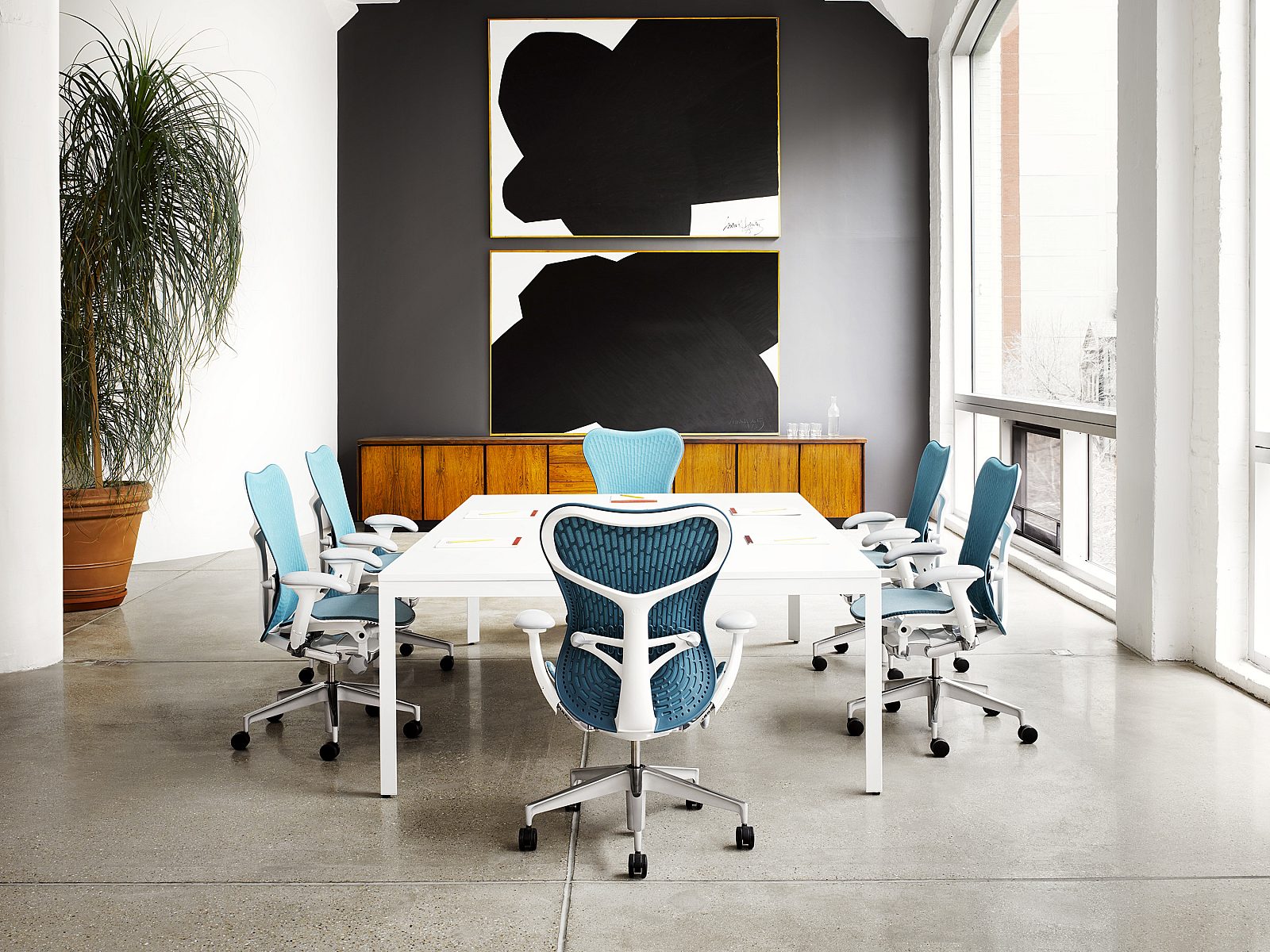 A conference room with blue Herman Miller Mirra 2 chairs, a white Layout Studio table and a large painting in the background.