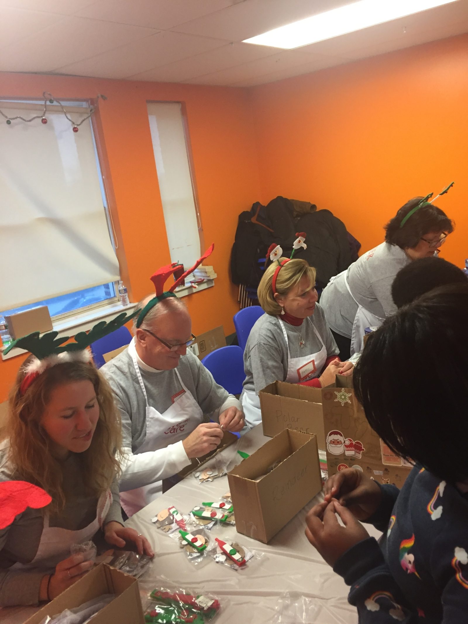 Premier employees assisting children in creating holiday crafts for their family. Premier employees are wearing holiday reindeer headbands.