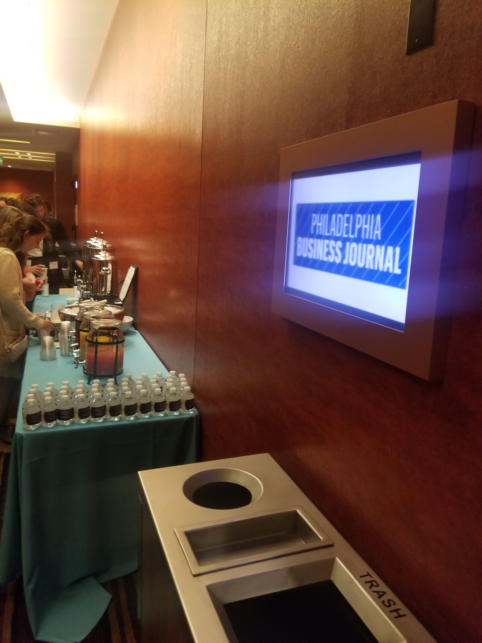 Lobby of convention center with table of refreshments. TV on wall with Philadelphia Business Journal's logo projected.