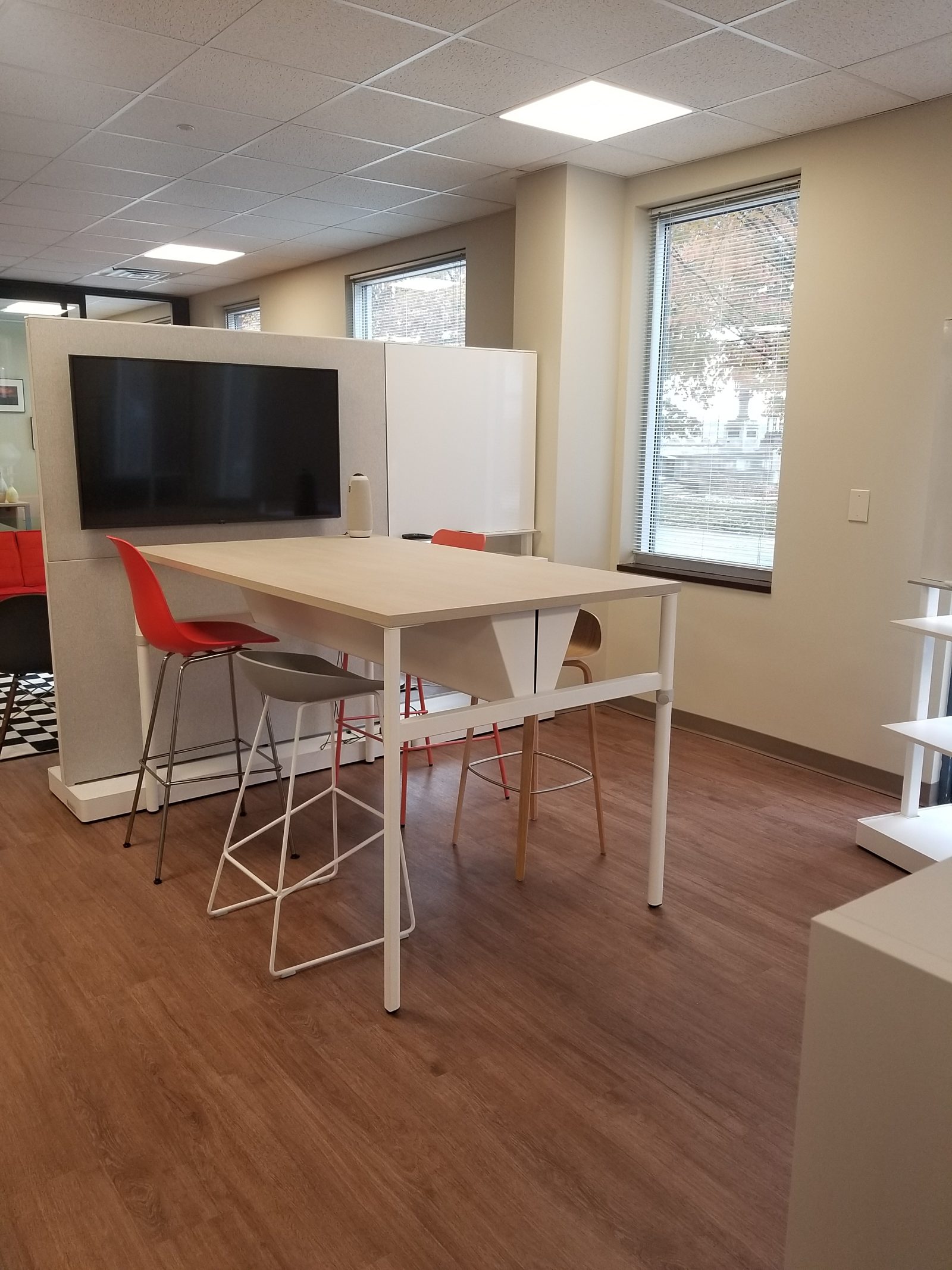 Bar-height collaborative table with a variety of 4 stools around it; Herman Miller OE1 Agile Walls behind table, one with a large TV screen attached.