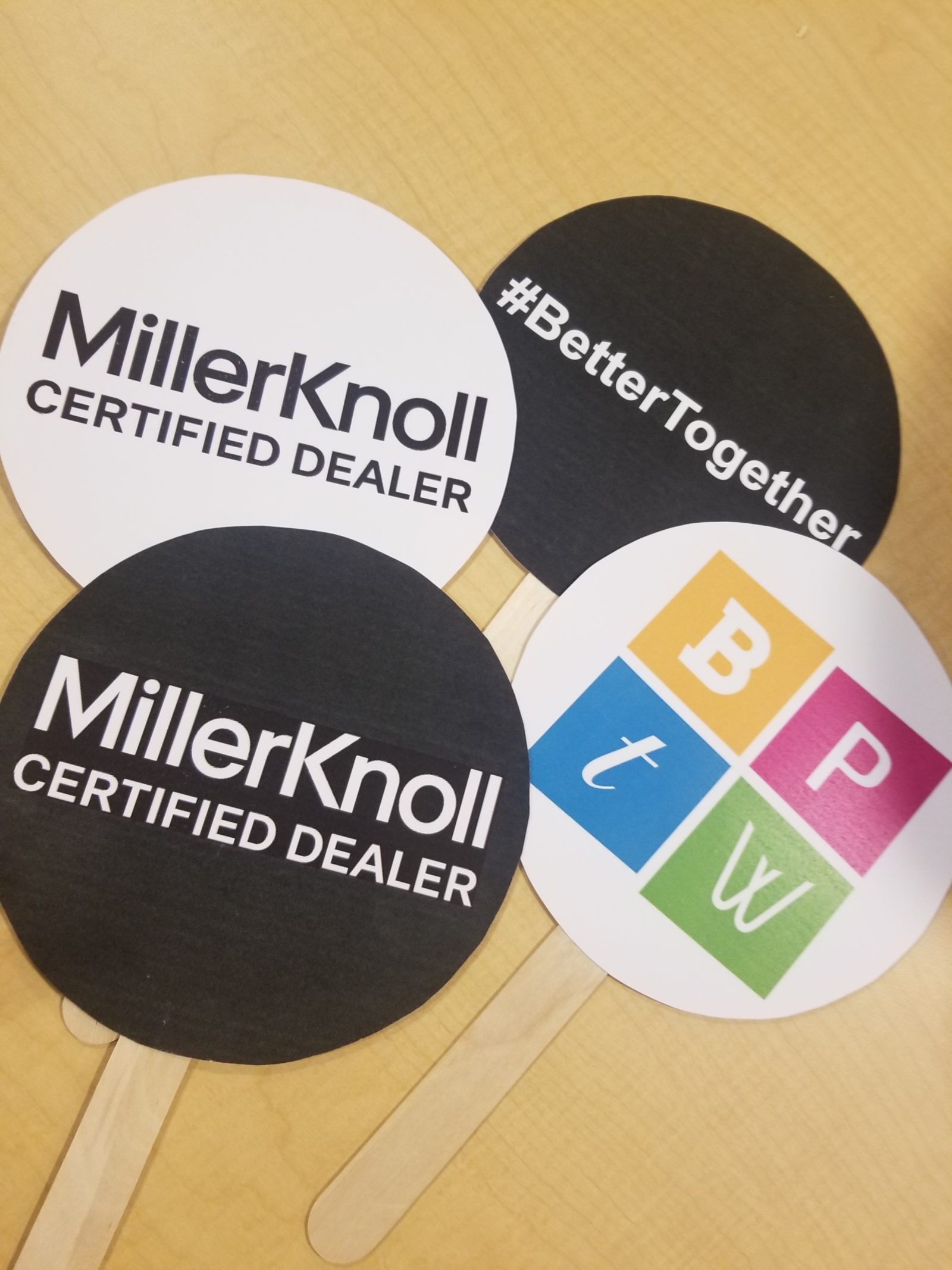 4 round signs with handles showing different images on each: MillerKnoll Certified Dealer logo, Best Places to Work logo and #BetterTogether