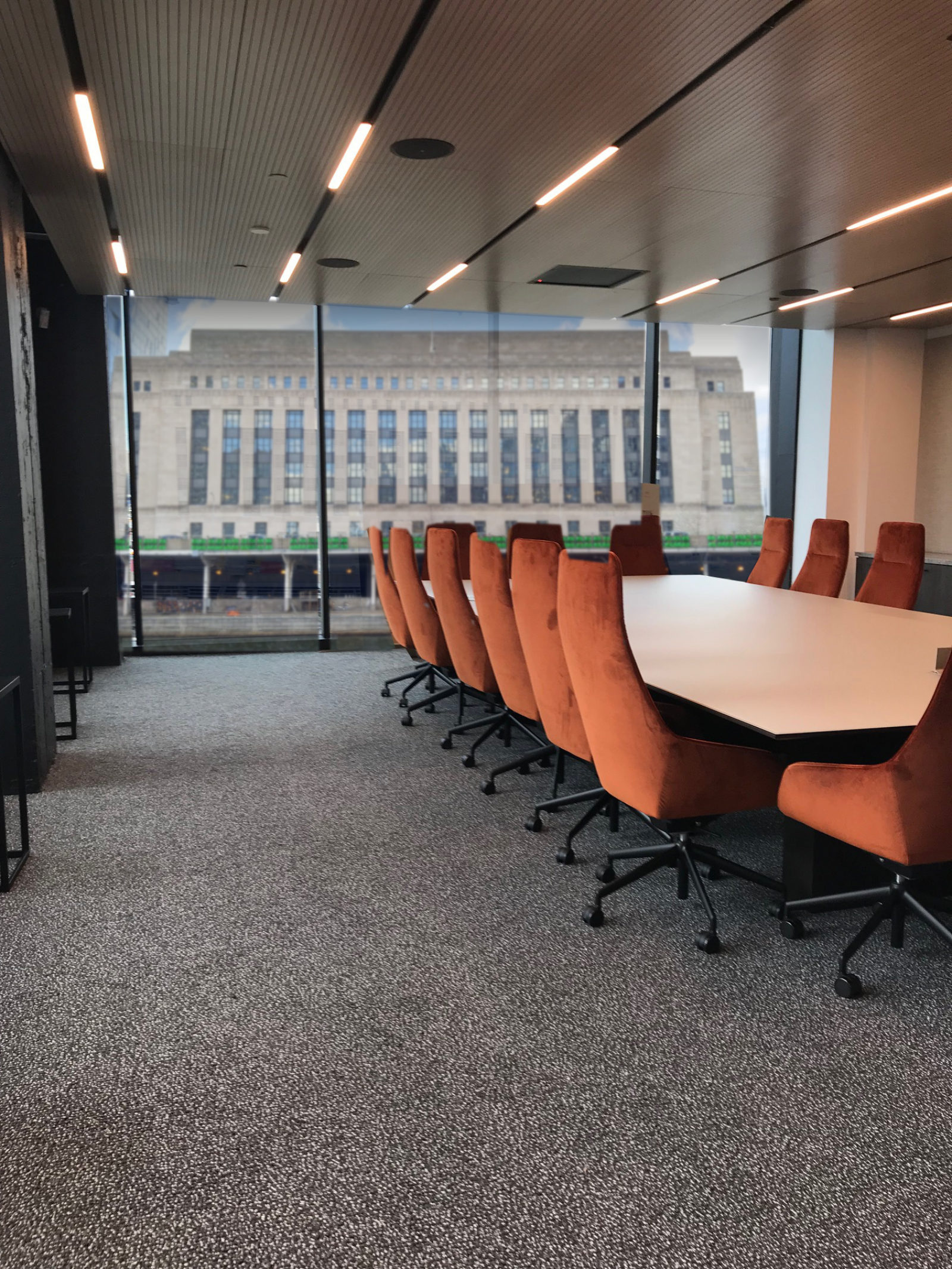 Conference room with burnt orange velvet chairs and a white table. View of the city in the background in the full-size windows.