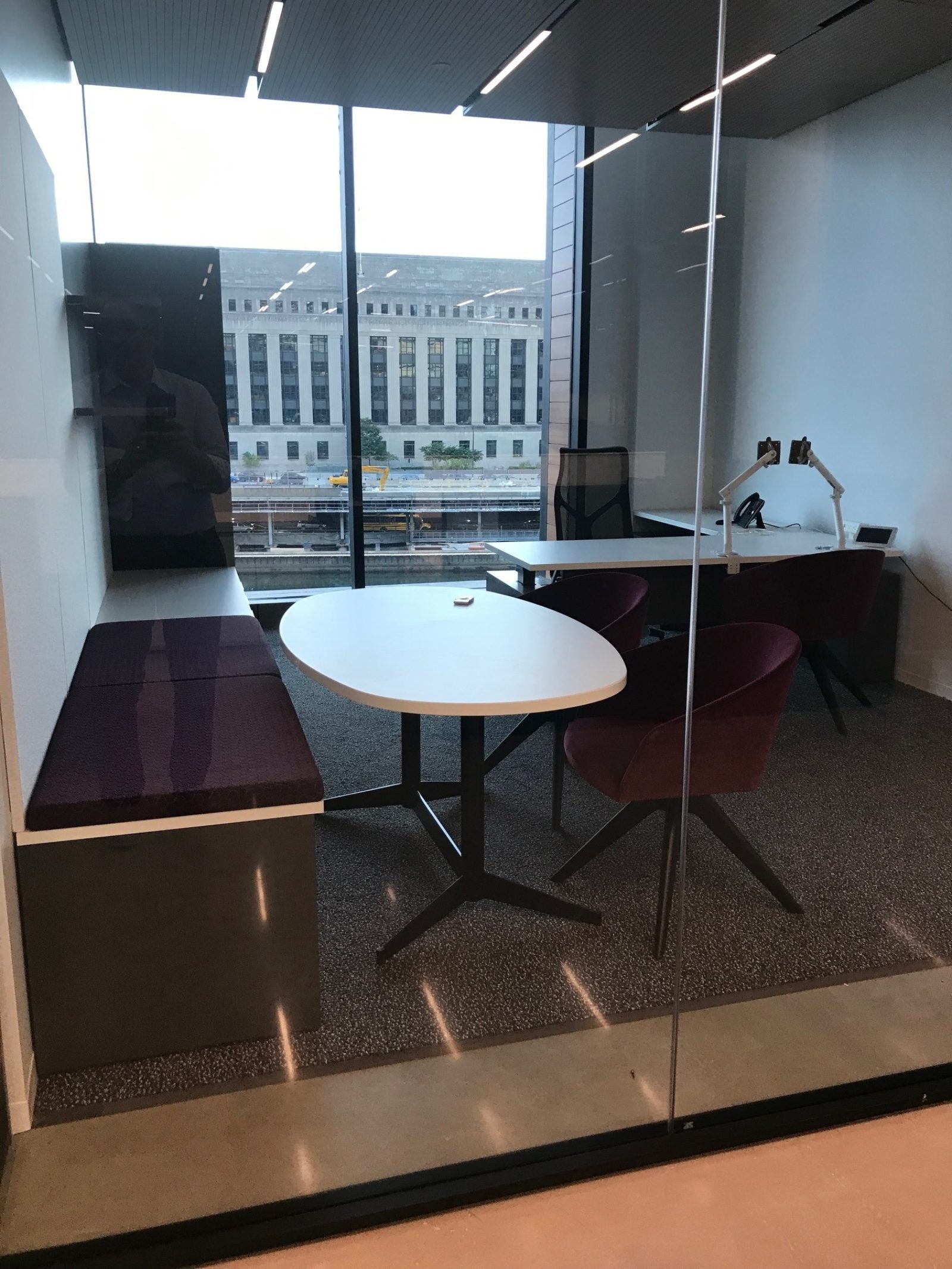 Private office with an L-shape desk on the right, an oval table on the left with bench seating.