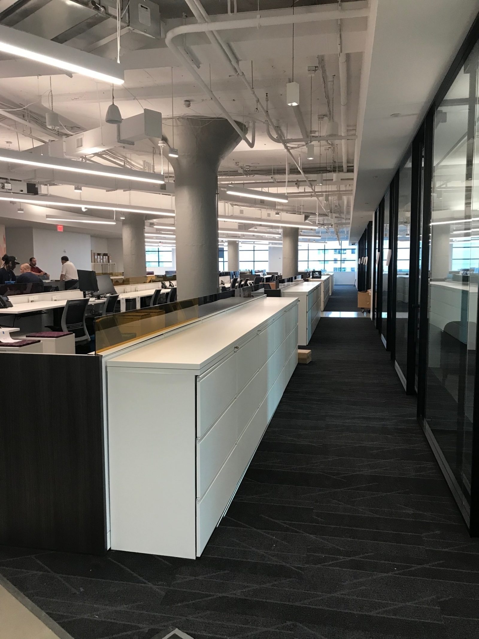 Modern office space showing hallway lined with lateral files, adjacent to a row of glass doors and walls.