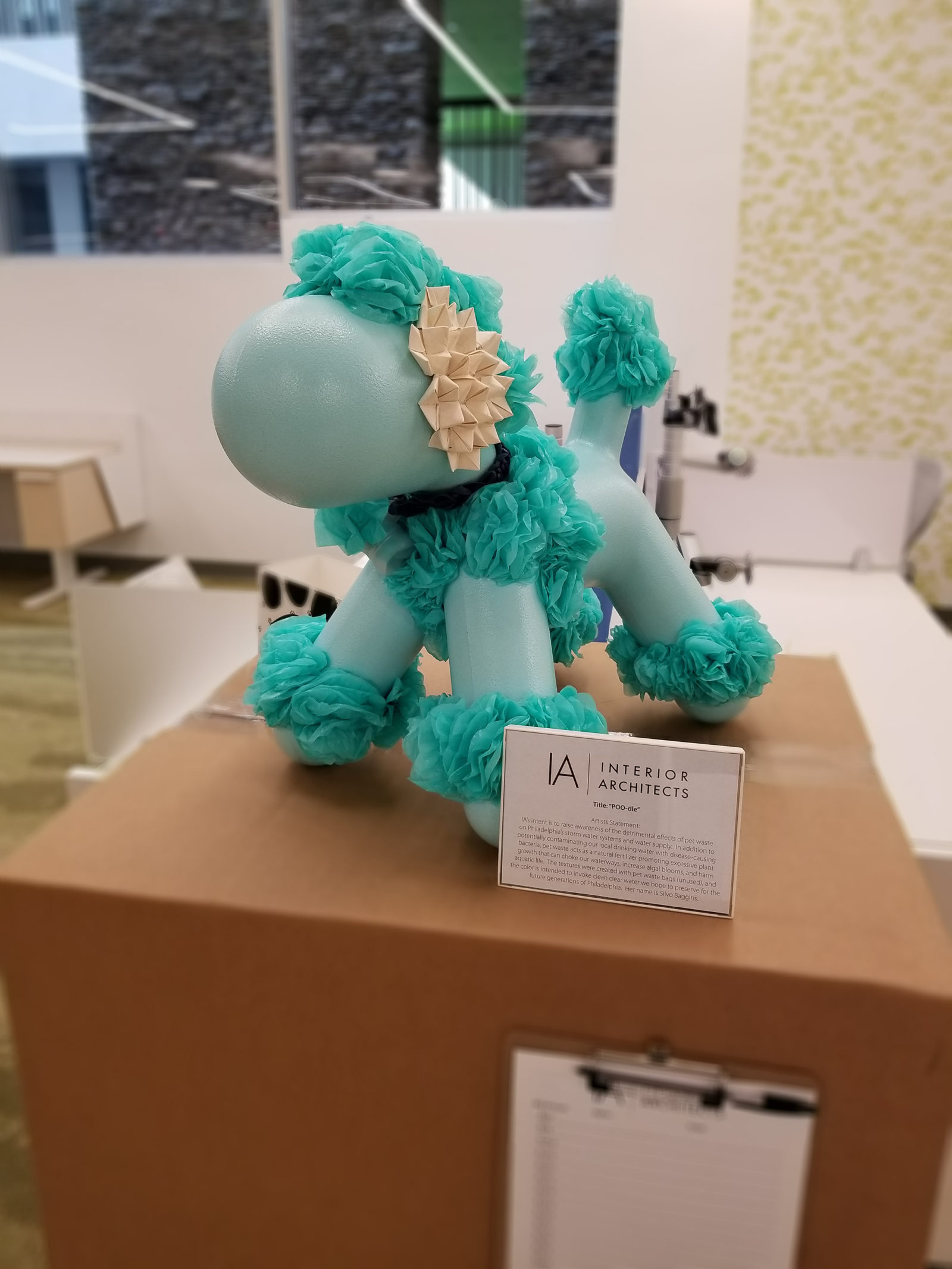 Dog statue painted a light blue/teal, then decorated with bright teal tulle around its feet, tail and on top of its head. It looks like a poodle.