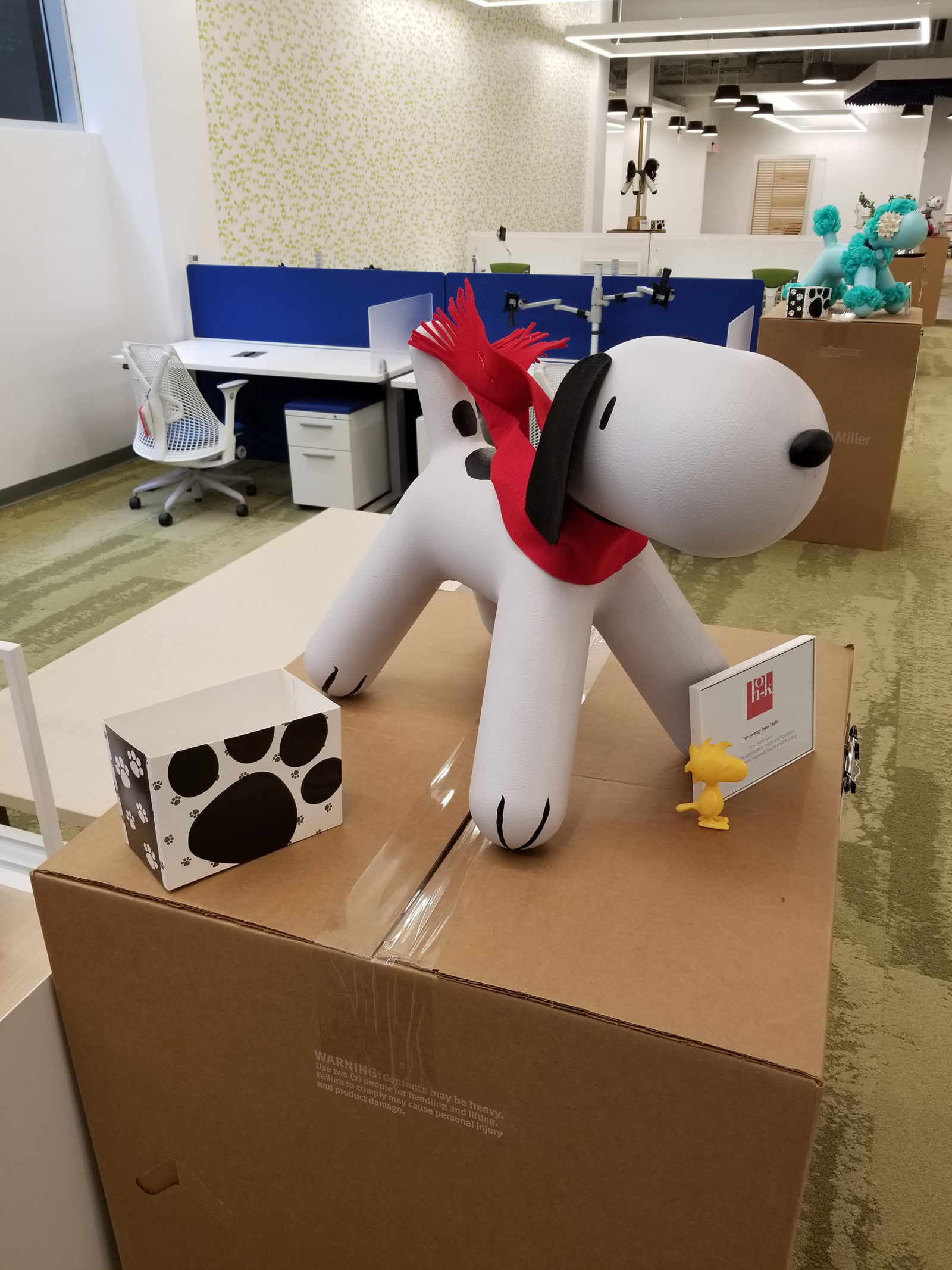 Dog statue with black floppy ears attached, a black nose, a few painted black spots and a red scarf around its neck. The dog resembles Snoopy.
