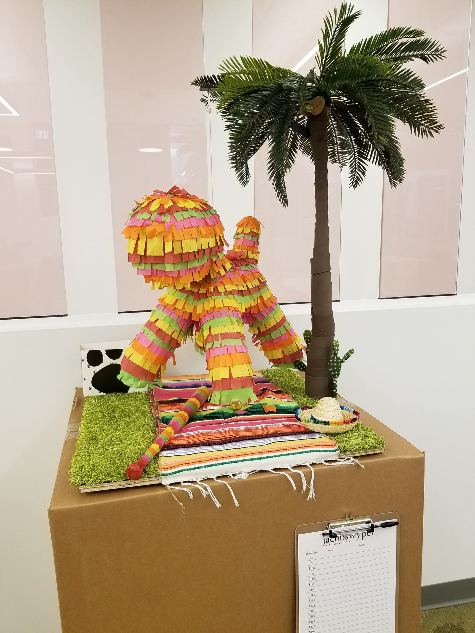 Cinco de mayo inspired setting with dog decorated like a piñata, next to a palm tree, mini sombrero and striped blanket.